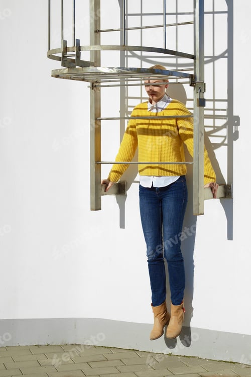 Preview: Girl in white shirt sticking out under yellow sweater and blue jeans posing near fire escape.