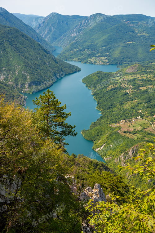 Preview: Canyon river meandering among green forested mountains, nature landscape photography under blue sky