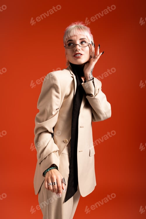 Preview: Young beautiful woman in stylish attire poses gracefully against a vibrant orange backdrop