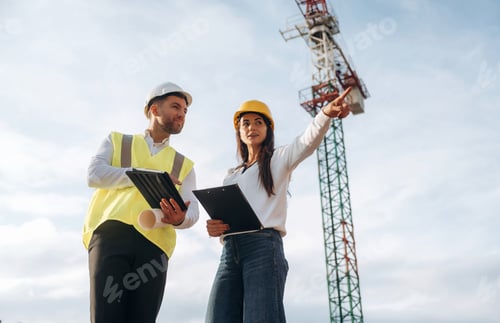 Preview: Man and woman, construction site workers are against crane, communication