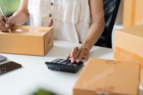 Preview: Small Business Owner Calculating finance and Managing Online Order with Cardboard Boxes on Desk