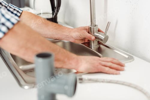 Preview: Selective focus of plumber fixing kitchen faucet near pipes on worktop
