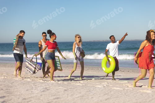 Preview: Front view of group of happy diverse friends walking together on the beach
