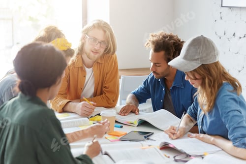 Preview: Group of students sitting together at table preparing for exam writing notes and reading books using