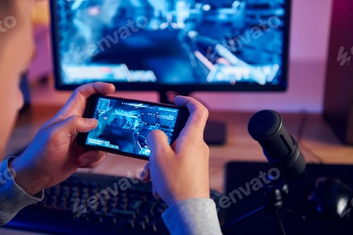 Preview: Using the smartphone. Online streamer playing FPS shooter game at home