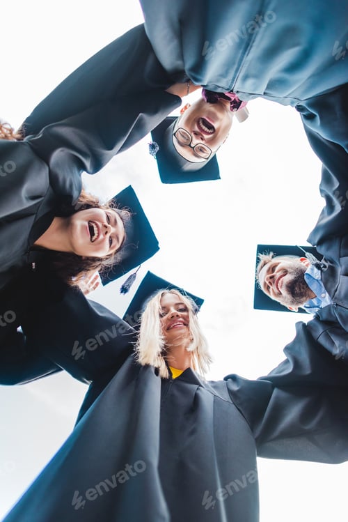 Preview: bottom view of cheerful multiracial graduates standing in row and looking at camera