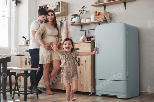 Preview: Playful female child have fun by running in the kitchen at daytime of front of her mother and father