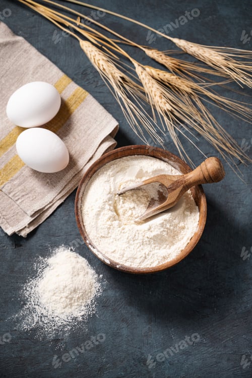 Preview: Wheat flour in a wooden bowl with a scoop and eggs on a dark background