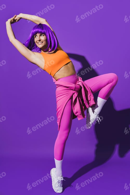 Preview: Carefree woman dancer wearing colorful sportswear performing against purple background