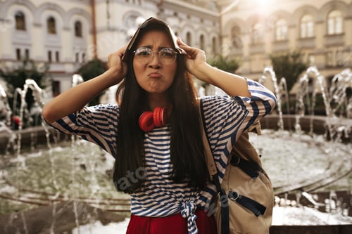 Preview: Sad funny woman in eyeglasses, striped shirt and red skirt looks into camera and covers head with m