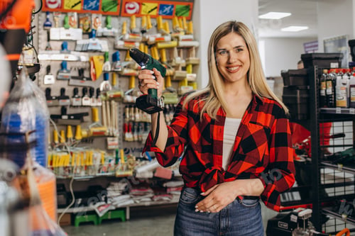 Preview: Beautiful smiling saleswoman is selling a drill at hardware store.