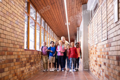 Preview: Female teacher with diverse group of students standing in school hallway, smiling