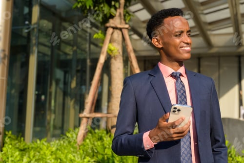 Preview: Portrait of successful young African businessman wearing suit and tie while using mobile phone