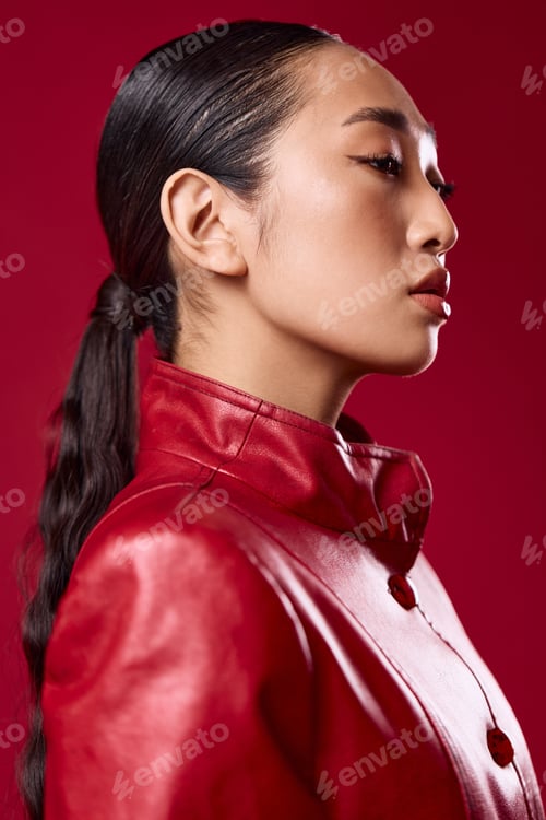 Preview: Fashion asian brunette woman in red leather jacket with ponytail hair, looking sideways with closed