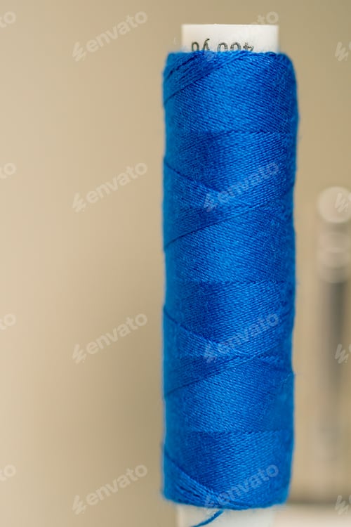 Preview: close-up in a sewing workshop of standing new white spool of light blue thread