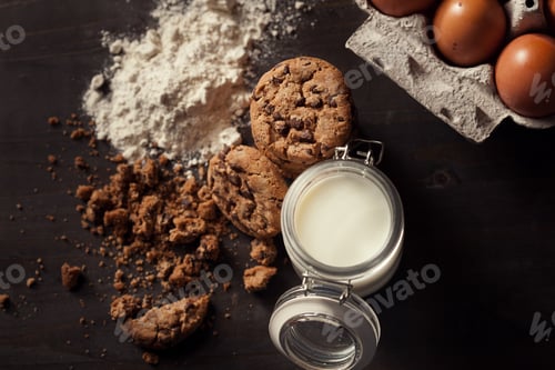 Preview: Top view of Homemade chocolate chip cookies with bottle of milk, white flour, fresh eggs and crumbs