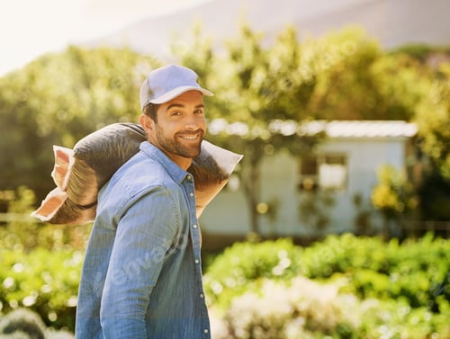 Preview: Portrait of a happy young farmer carrying a bag of compost over his shoulder on the farm