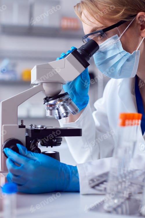Preview: Close Up Of Female Lab Worker Wearing PPE And Safety Glasses Looking At Slide Under Microscope
