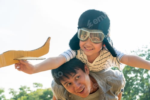 Preview: Asian boy wearing pilot helmet playing airplane toy on father back at park