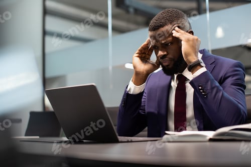 Preview: Concentrated black businessman solving business tasks, using computer