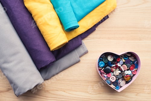 Preview: top view of wooden table with rolls of fabric and heart shaped box with buttons