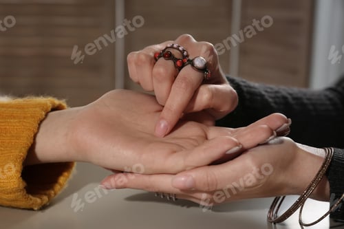 Preview: Chiromancer reading lines on woman's palm at table, closeup
