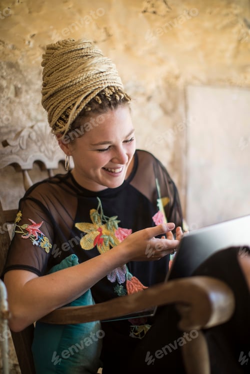 Preview: Portrait of young woman with dreadlocks, sitting outdoors, using digital tablet