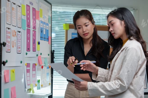Preview: Two female ux/ui designers engaging in a discussion about mobile app interface design, utilizing wir