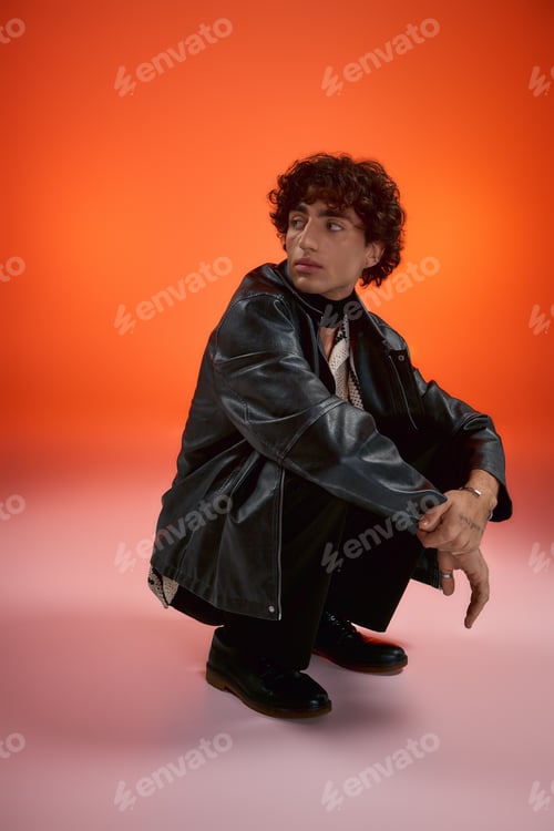 Preview: Stylish young man poses confidently in a trendy outfit against a vibrant orange background