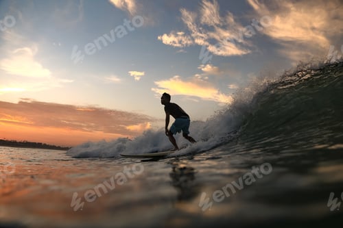 Preview: Man on surf board on waving water at sunset