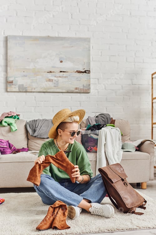Preview: smiling and fashionable woman in straw hat and sunglasses sitting on floor with leather bag