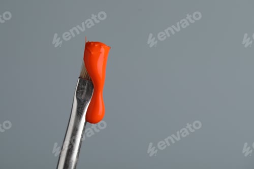 Preview: Brush with orange paint on light grey background, closeup. Space for text