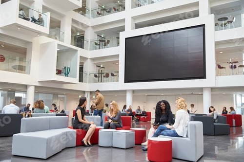 Preview: Students sit talking under AV screen in atrium at university