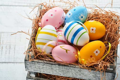 Preview: Easter holiday. Colorful Easter eggs in wooden basket on white wooden background. Easter greeting ca