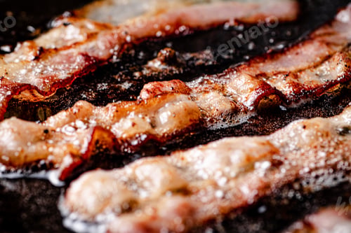 Preview: Pieces of bacon are fried in boiling oil with air bubbles.