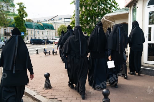 Preview: Many nuns in black dresses walking on the street, back view.