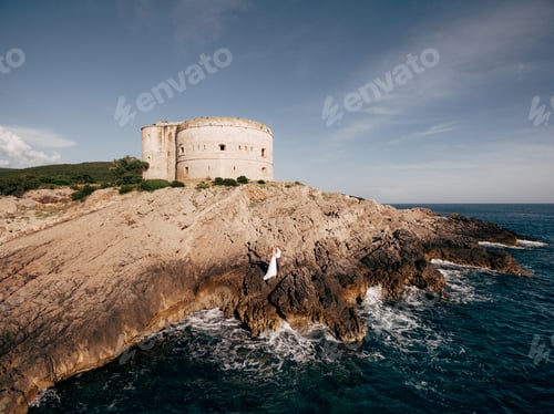 Preview: The bride and the groom stand embracing and holding hands on the rocky seashore near Arza fortress