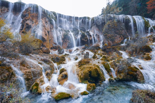 Preview: Waterfall flowing over mossy rocks in serene forest landscape with autumn colors