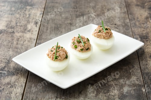 Preview: Deviled eggs with tuna and chives resting on a white rectangular plate on rustic wooden table