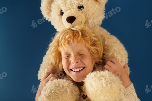 Preview: Blonde boy joyfully embraces a fluffy teddy bear against a blue backdrop