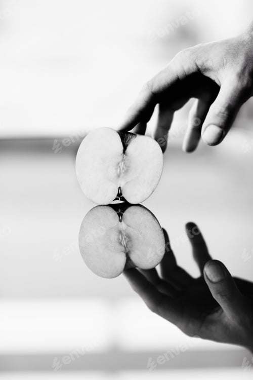 Vorschau: Eine Hand, die einen halben Apfel gegen eine glänzende Oberfläche hält, auf der sich die Spiegelung befindet