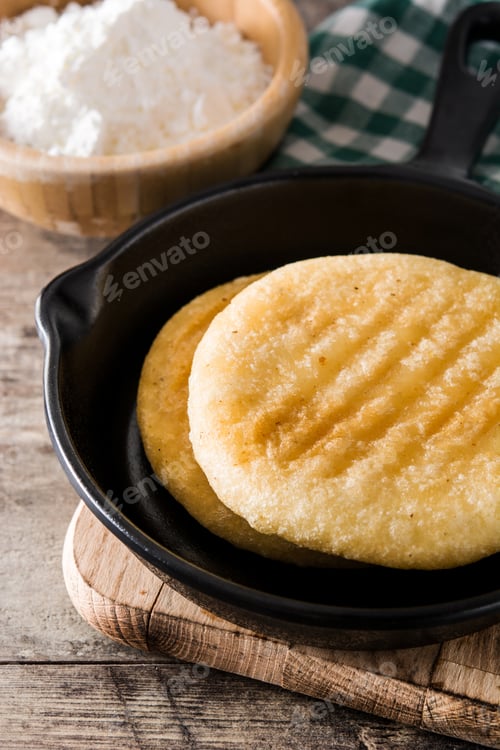 Preview: Delicious arepas resting in frying pan with precooked corn flour in background