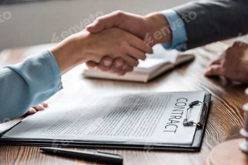 Preview: close-up view of clipboard with contract and lawyer with client shaking hands behind