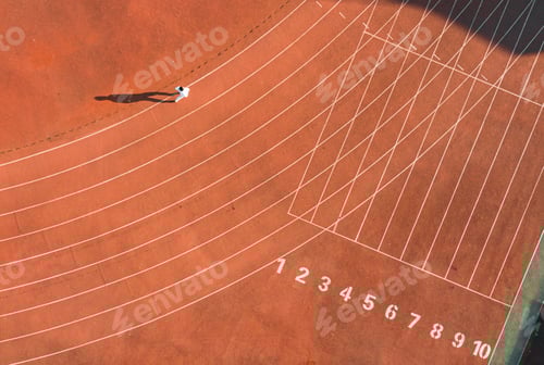 Preview: Young man standing on an outdoor tennis court, with a shadow cast on the ground beneath them