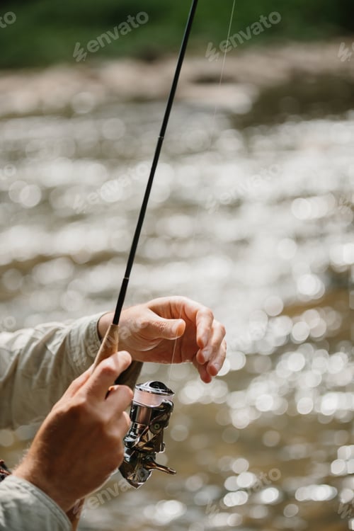 Preview: Fisherman reeling line on spinning rod in river for trout fishing
