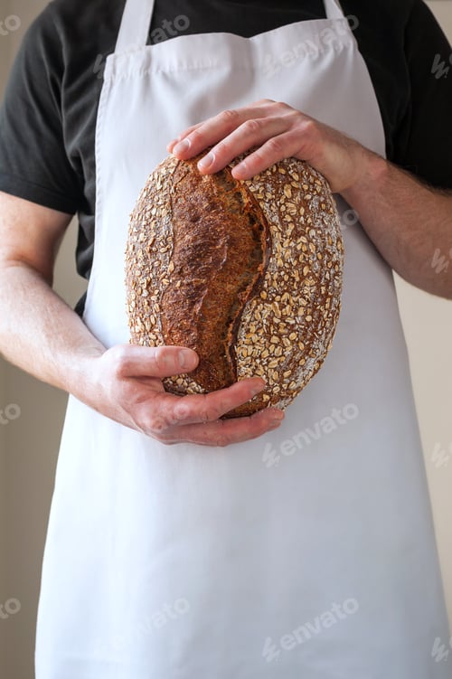 Preview: Close-up at bakers hands holding a loaf of bread in front of him.