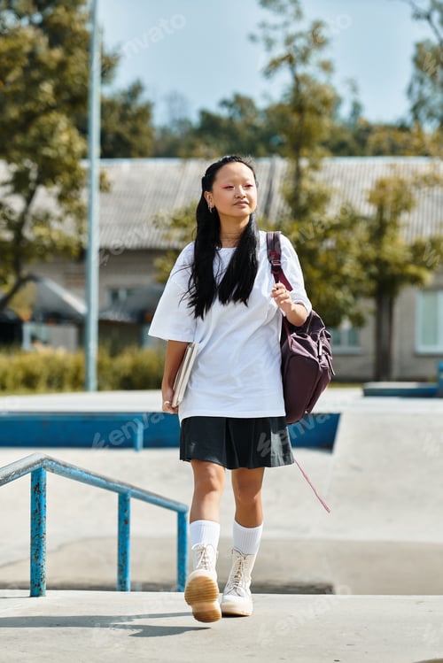 Preview: A stylish young Asian student walks confidently at a skatepark during a sunny afternoon