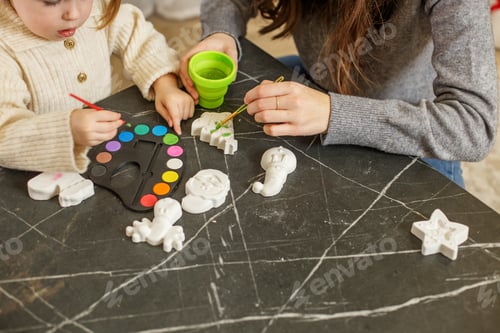 Preview: Child painting Christmas decorations at home with parent during holiday season