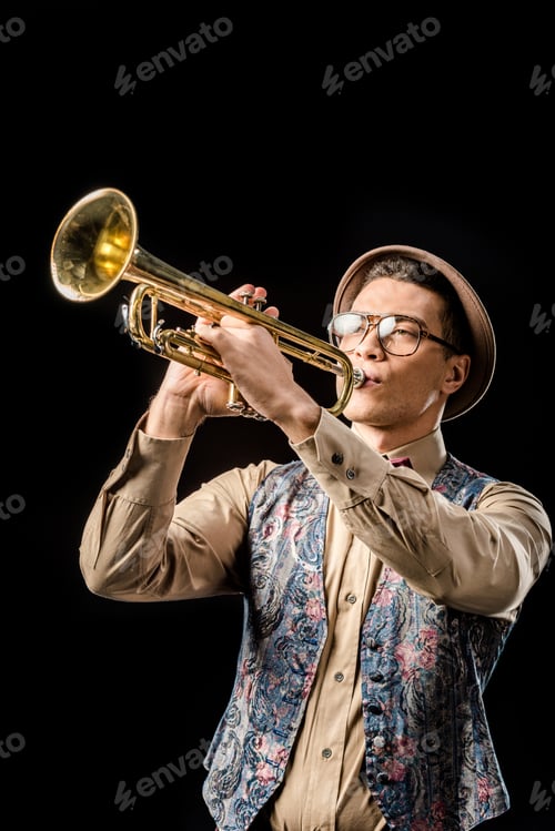 Preview: handsome male jazzman in hat and eyeglasses playing on trumpet isolated on black