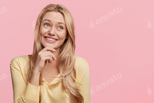 Preview: Dreamful pretty blonde woman with long hair has appealing smile, looks thoughtfully aside, poses aga